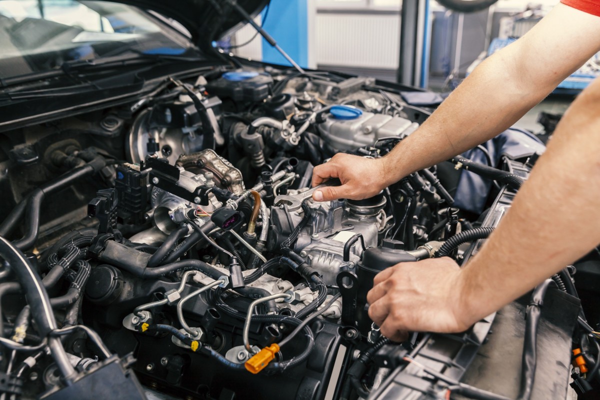 mechanic's hands holding wrench under the hood of a car 